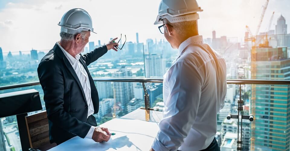 Two people at a construction site with blueprints and construction hats